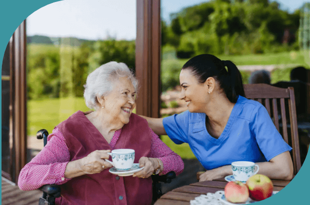 Elderly woman and caregiver enjoying tea outdoors.